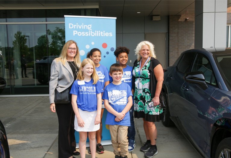 STEM students standing with adults in front of a sign reading driving possibilities