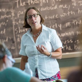 Teacher teaching to class with chalkboard behind her